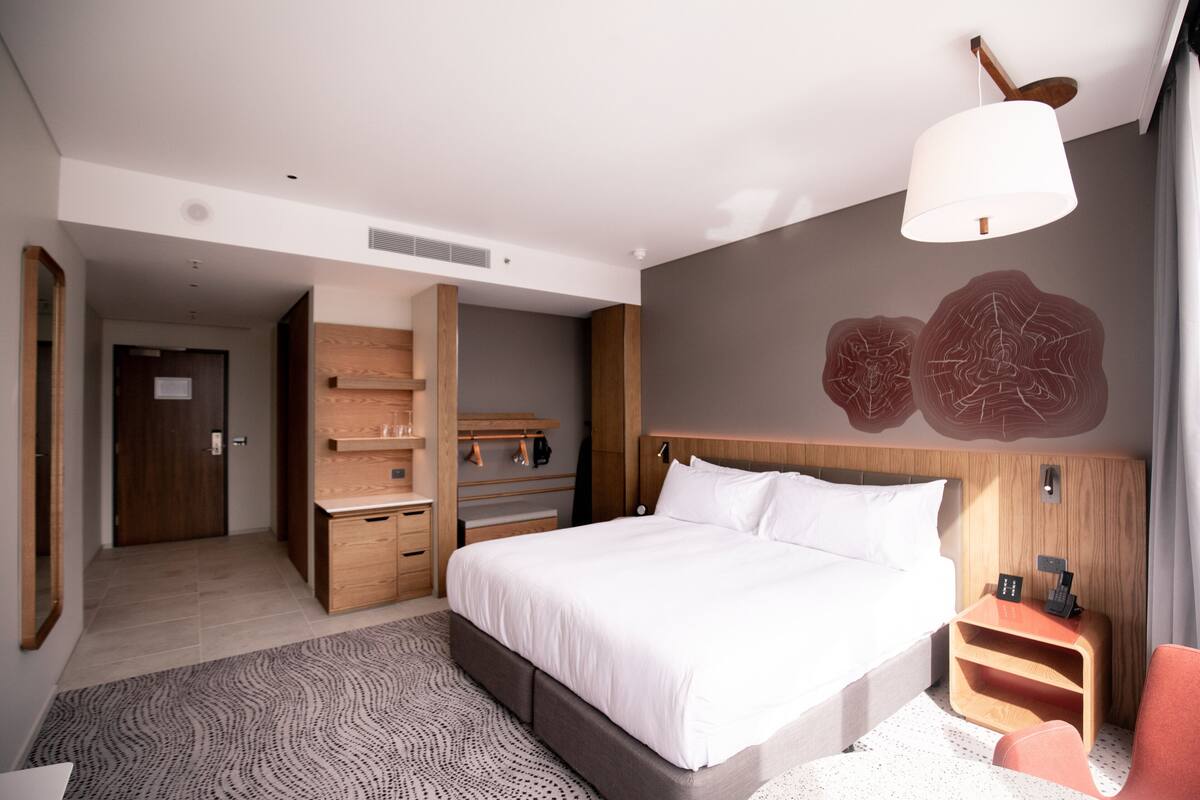 Ett modernt hotellrum med en stor säng, ett träbeklätt sänggavel, ett nattduksbord med en lampa och en inbyggd garderob.