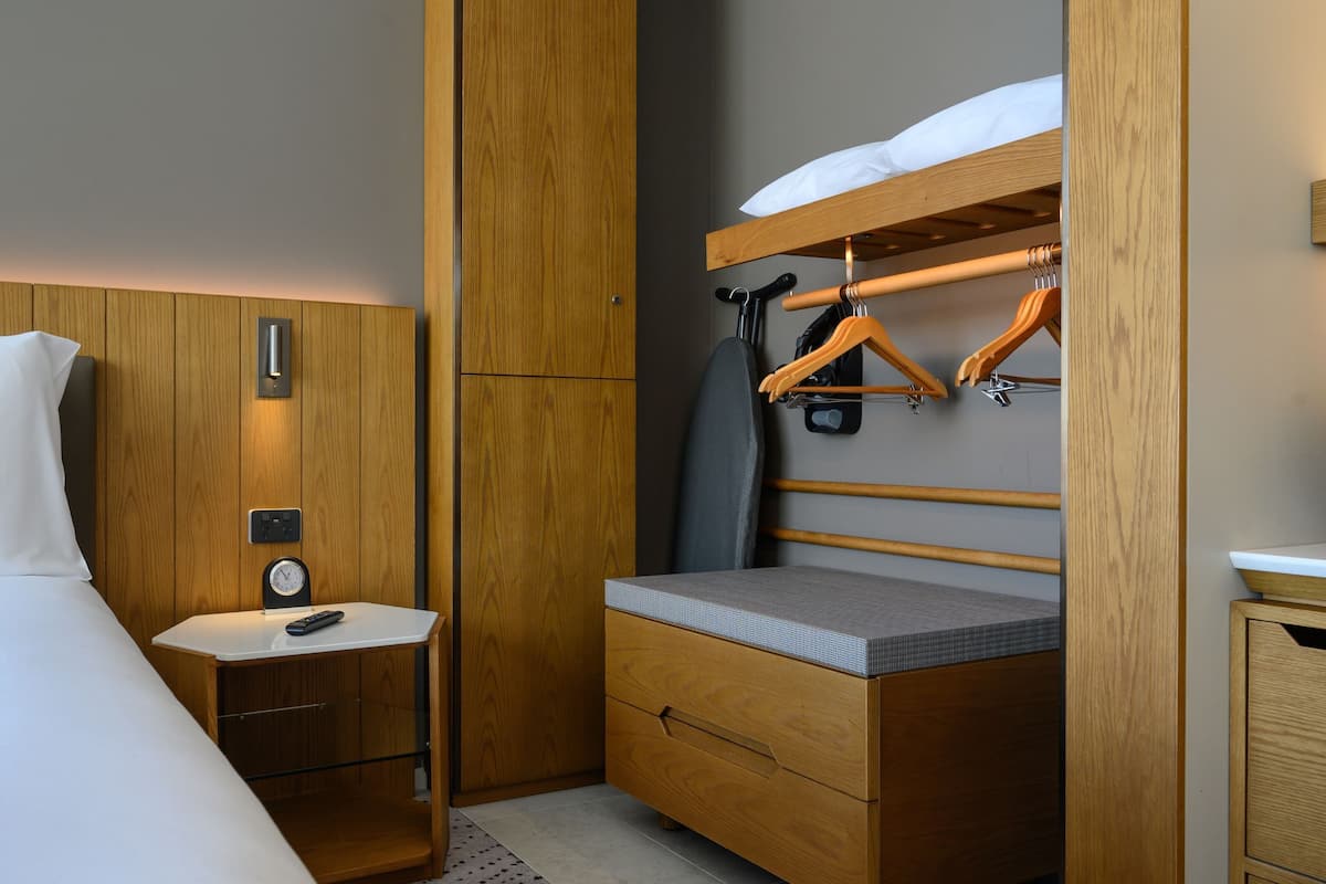 Een kleine hotelkamer met een stapelbed, een nachtkastje met een klok en een kleine kledingkast.