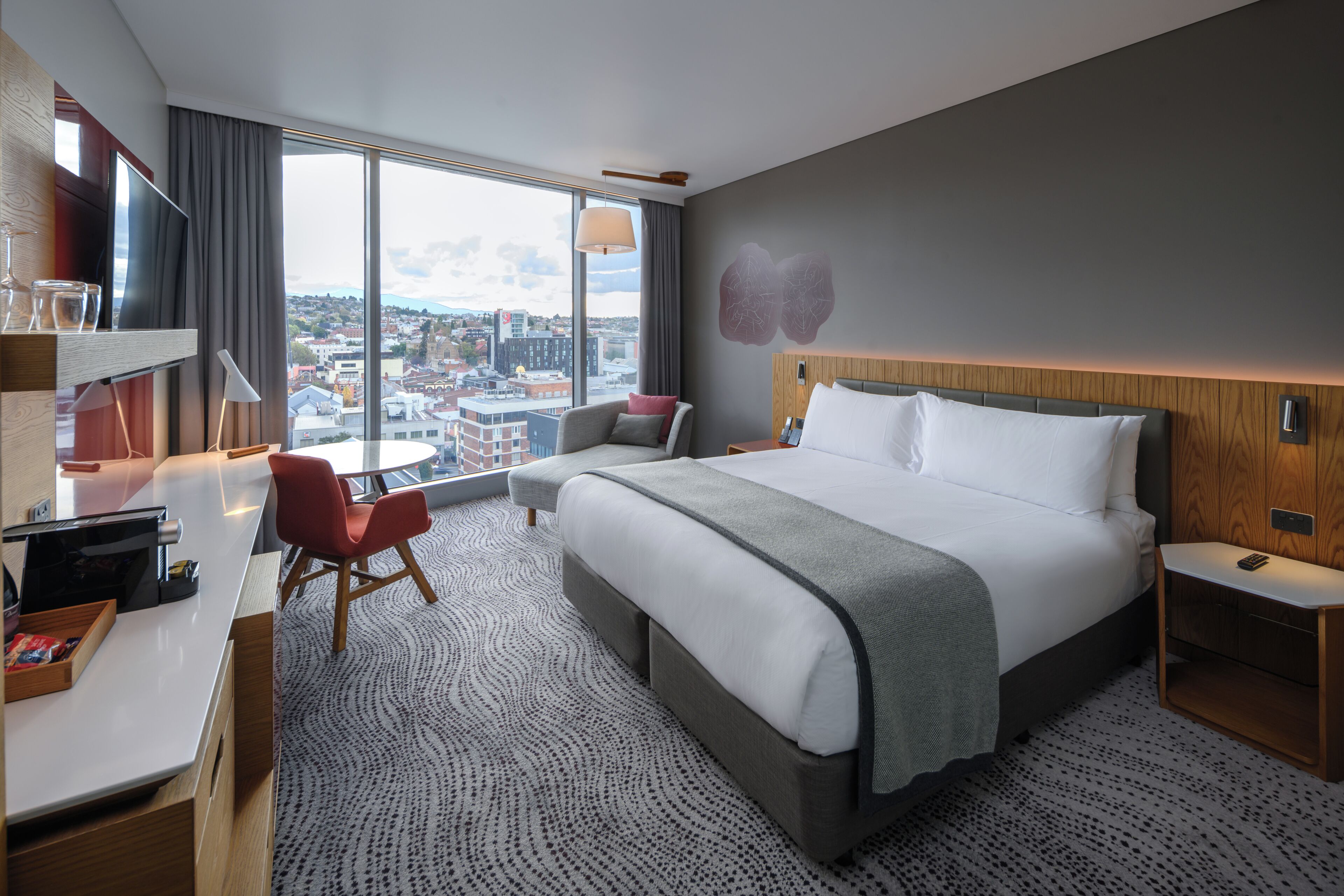 Une chambre d’hôtel moderne dotée d’un grand lit, d’un bureau, d’une chaise, d’une table de chevet et offrant une vue sur la ville.