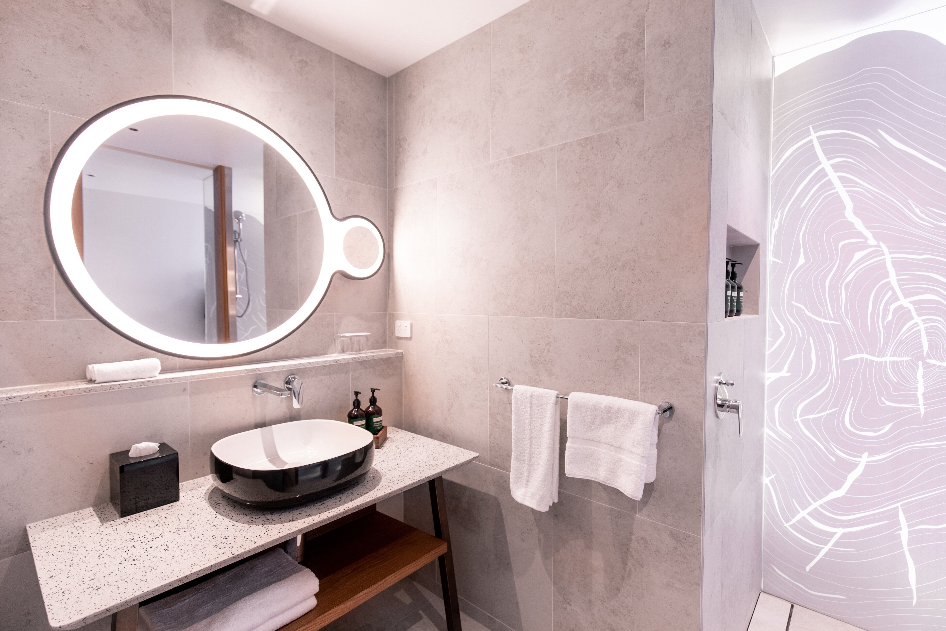 Une salle de bain moderne avec un grand miroir rond, un lavabo et une douche.