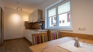A small kitchen with wooden cabinets, a coffee machine, and a window with blinds. - Rotflüh - Apartments Steffi (Tannheim)