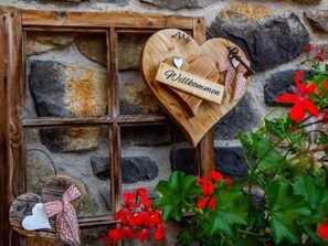 A stone wall with a wooden window frame and a heart-shaped wooden sign with the name 'Wilkommen'.