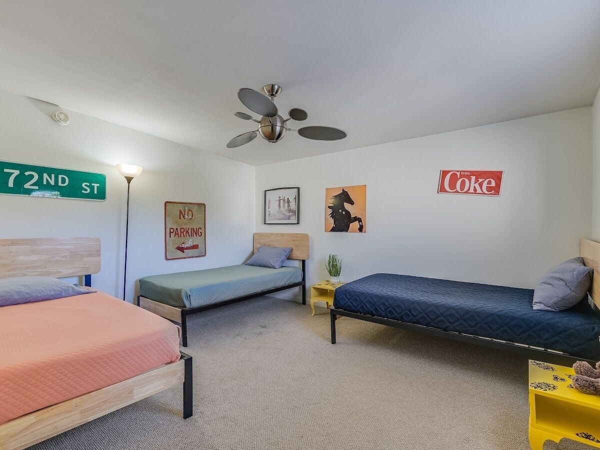 Habitación tipo dormitorio con tres camas, un ventilador de techo, un letrero de 'No Estacionar' y un anuncio de 'Coke' en la pared.