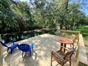 Una terraza de madera con una mesa y sillas, con vistas a un cuerpo de agua tranquilo y rodeada de árboles.