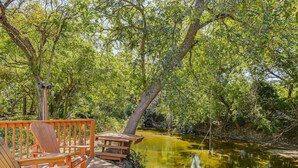 A wooden deck with Adirondack chairs and a picnic table overlooking a pond.
