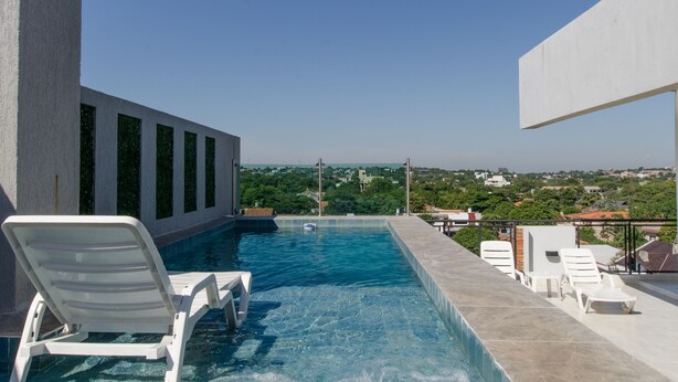 Uma piscina infinita com espreguiçadeiras brancas, vista desobstruída da paisagem urbana e design arquitetônico moderno.