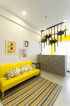Un sofá amarillo brillante con cojines estampados, un tapete a rayas y decoración en la pared que incluye un diseño de ojo y un cohete.