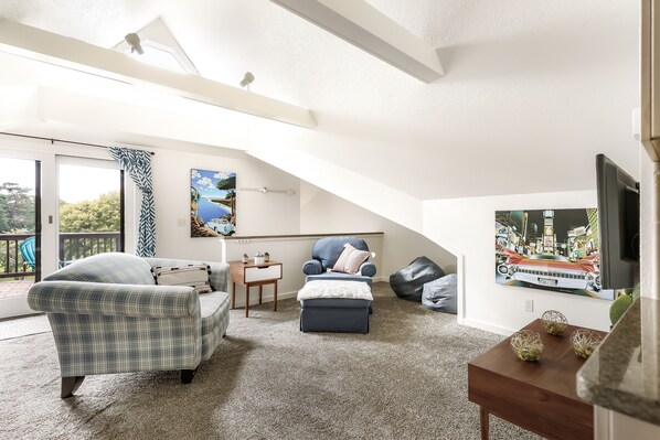 Un salón tipo loft con techo alto, un ventanal grande, un sofá, una silla, una mesa de centro y un televisor.
