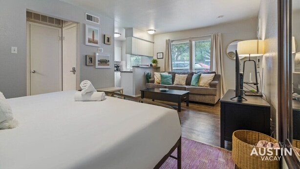A hotel room with a bed, a sofa, a coffee table, a lamp, and a small kitchen area. - Enfield #114 xxxxxxx (Austin)