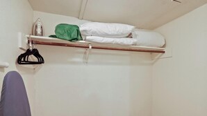 A small, clean room with a bed, a hanging rack, and a shelf with a green hat and rolled-up white towels. - Enfield #114 xxxxxxx (Austin)