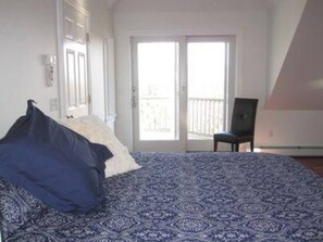 Un dormitorio con una colcha estampada, una silla y una puerta al balcón.