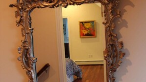 Uno specchio con una cornice elaborata che riflette una stanza con una coperta dal disegno vivace e un quadro appeso al muro.