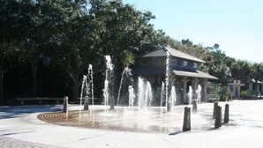 Une fontaine publique dotée de plusieurs jets d’eau, entourée d’une zone pavée dont le motif est constitué de briques.