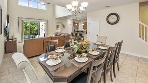 A spacious dining area with a large table set for six, a chandelier, and a view of the kitchen and dining room in the background. - Only Minutes to Disney (Kissimmee)
