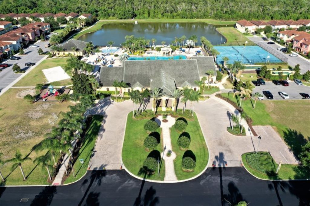 An aerial view of a residential area with a large swimming pool, multiple houses, and a small lake.