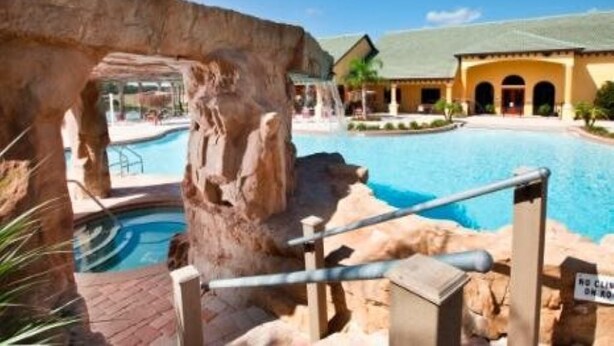 A pool area with a natural rock formation, a building with a green roof, and a sign indicating no climbing on rocks. - Only Minutes to Disney (Kissimmee)