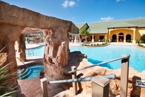 A pool area with a natural rock formation, a building with a green roof, and a sign indicating no climbing on rocks.