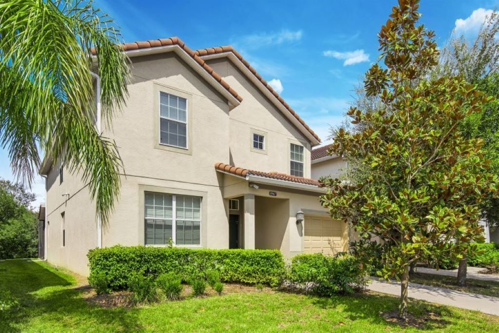 A two-story house with a beige exterior, a front porch, and a well-maintained lawn.