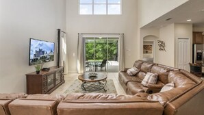A spacious living room with a leather sofa, a coffee table, and a television on the wall. - Only Minutes to Disney (Kissimmee)