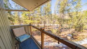 A balcony with a wooden railing, a blue patterned sofa, and a view of a forested area. - Family-Friendly, Updated Condo w/Outdoor Pool (Keystone)