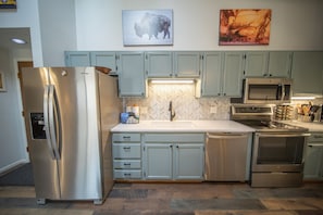A modern kitchen with stainless steel appliances, light blue cabinets, and a herringbone tile backsplash.