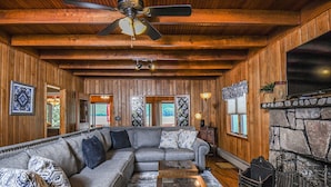 A cozy living room with a sectional sofa, a coffee table, a fireplace, and wooden walls.