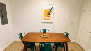 A dining area with a wooden table, four green chairs, and a woven placemat. - Sosuite | Arcade 2BR Apt w/ W/D (Philadelphia)