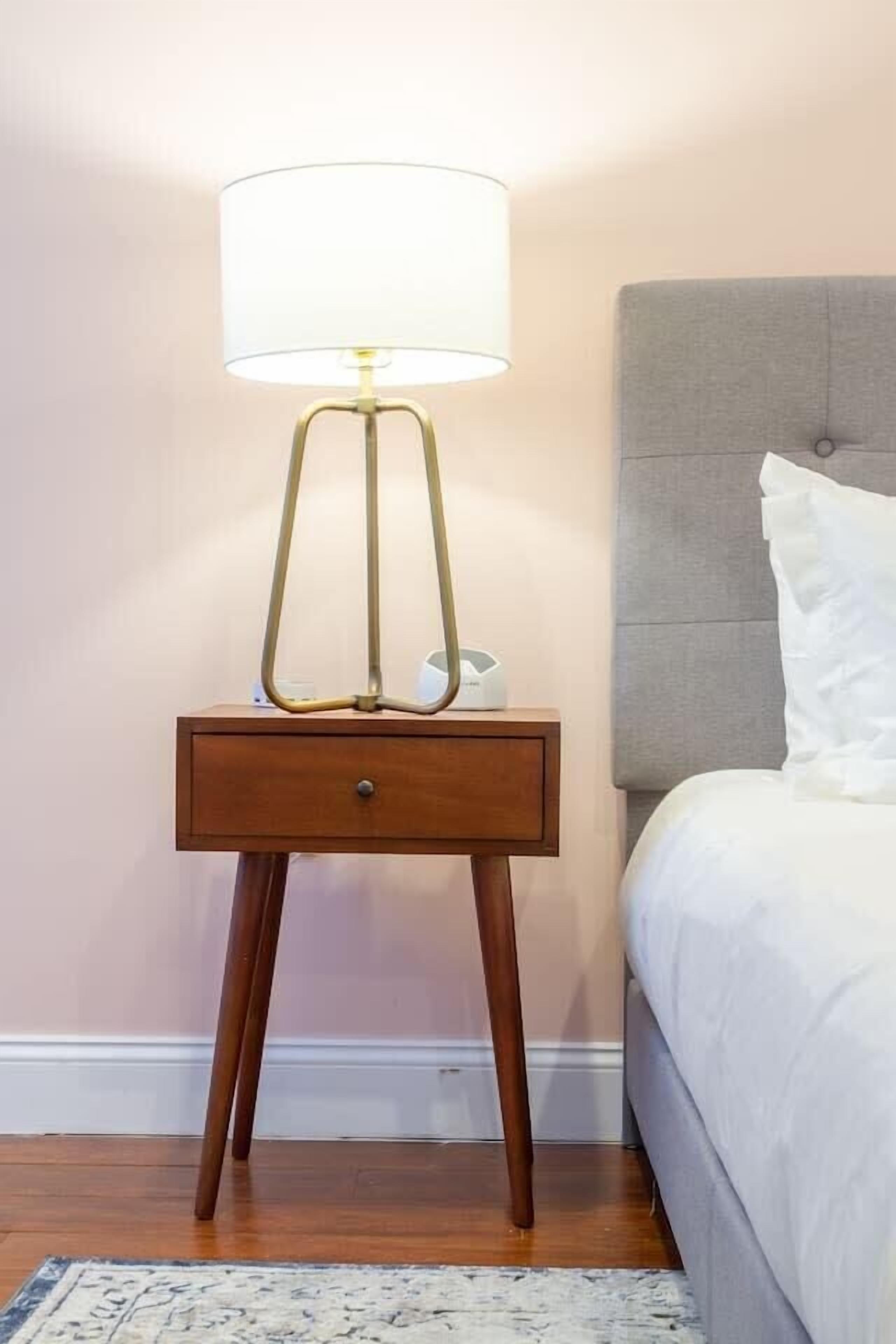 A bedside table with a lamp, a bedside drawer, and a bed with a headboard.