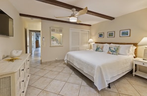 A bedroom with a bed, nightstands, a ceiling fan, a dresser, and a door leading to another room. - Beachfront!  Incredible Location, Amenities, and Views! (St. Thomas)