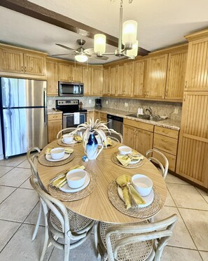 A kitchen with wooden cabinets, a stainless steel refrigerator, a microwave, and a dining table set with white bowls and napkins.