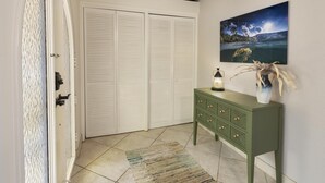 Una habitación con un armario blanco cerrado, un aparador verde con cajones, una mesita con una vela y un cuadro en la pared.