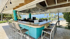 Un área de bar al aire libre con barra, taburetes y vistas a la playa.