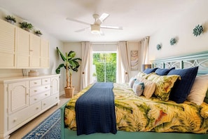 Une chambre à coucher avec un lit, un ventilateur de plafond, une fenêtre avec des rideaux, une plante en pot et une commode.