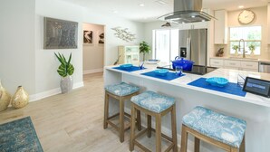 A modern kitchen with a central island, bar stools, and a stainless steel refrigerator. - Modern Coastal Pool Retreat • Private Heated Pool • Minutes to Siesta Key Beach (Sarasota)