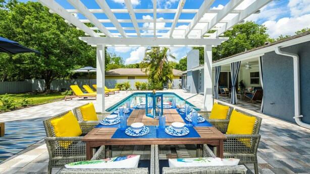 A covered outdoor dining area with a pool, wicker furniture, and a pergola. - Modern Coastal Pool Retreat • Private Heated Pool • Minutes to Siesta Key Beach (Sarasota)