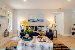 A living room with a dark blue sofa, a coffee table with a bottle holder, and a painting of sailboats on the wall.