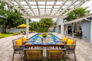 Un patio exterior con pérgola, mesa de billar acondicionada para comer y mobiliario de mimbre.