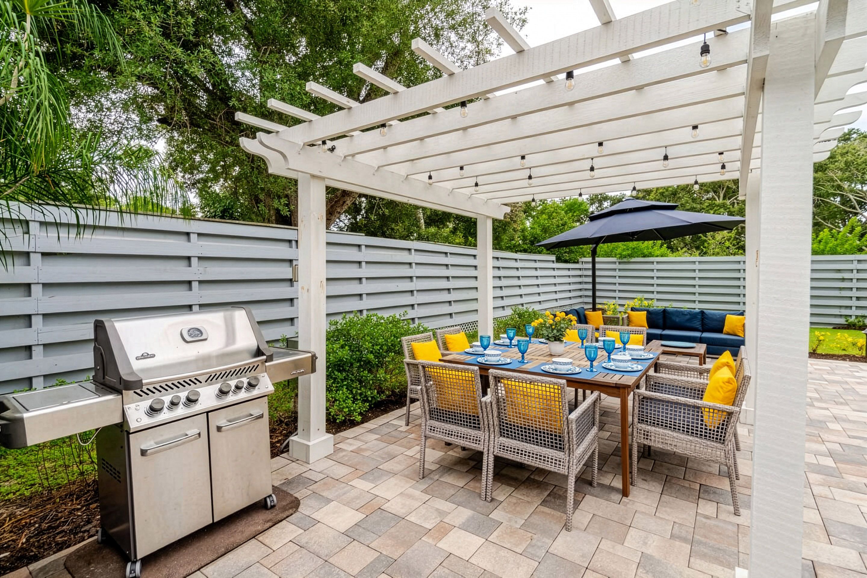 An outdoor patio with a grill, dining table, chairs, and an umbrella.