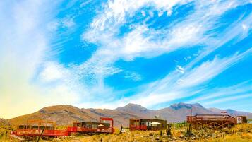 Paisaje desértico con una montaña al fondo y un edificio de techo rojo con varias habitaciones.