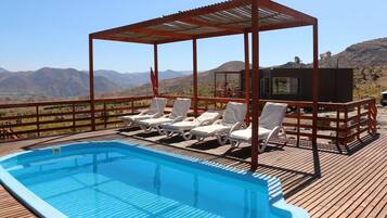 Una piscina con sillas de descanso y una pérgola, rodeada de montañas.