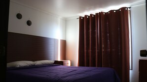 Een slaapkamer met een groot bed, een nachtkastje en een raam met gordijnen.
