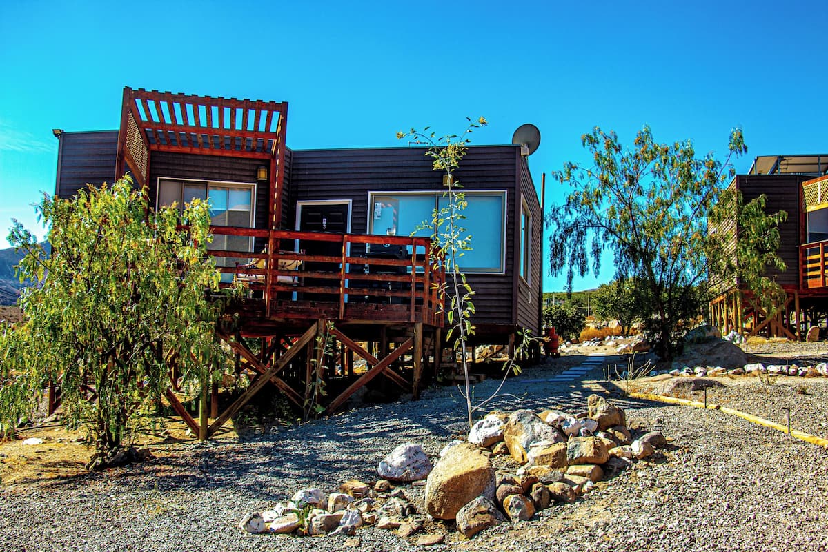 A wooden cabin with a deck, surrounded by rocks and sparse vegetation.