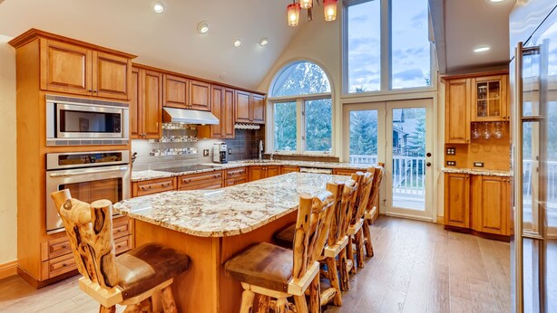A spacious kitchen with wooden cabinets, a large island with bar stools, and a view through the windows. - Breck Town Lodge | In Town | Walkability (Breckenridge)