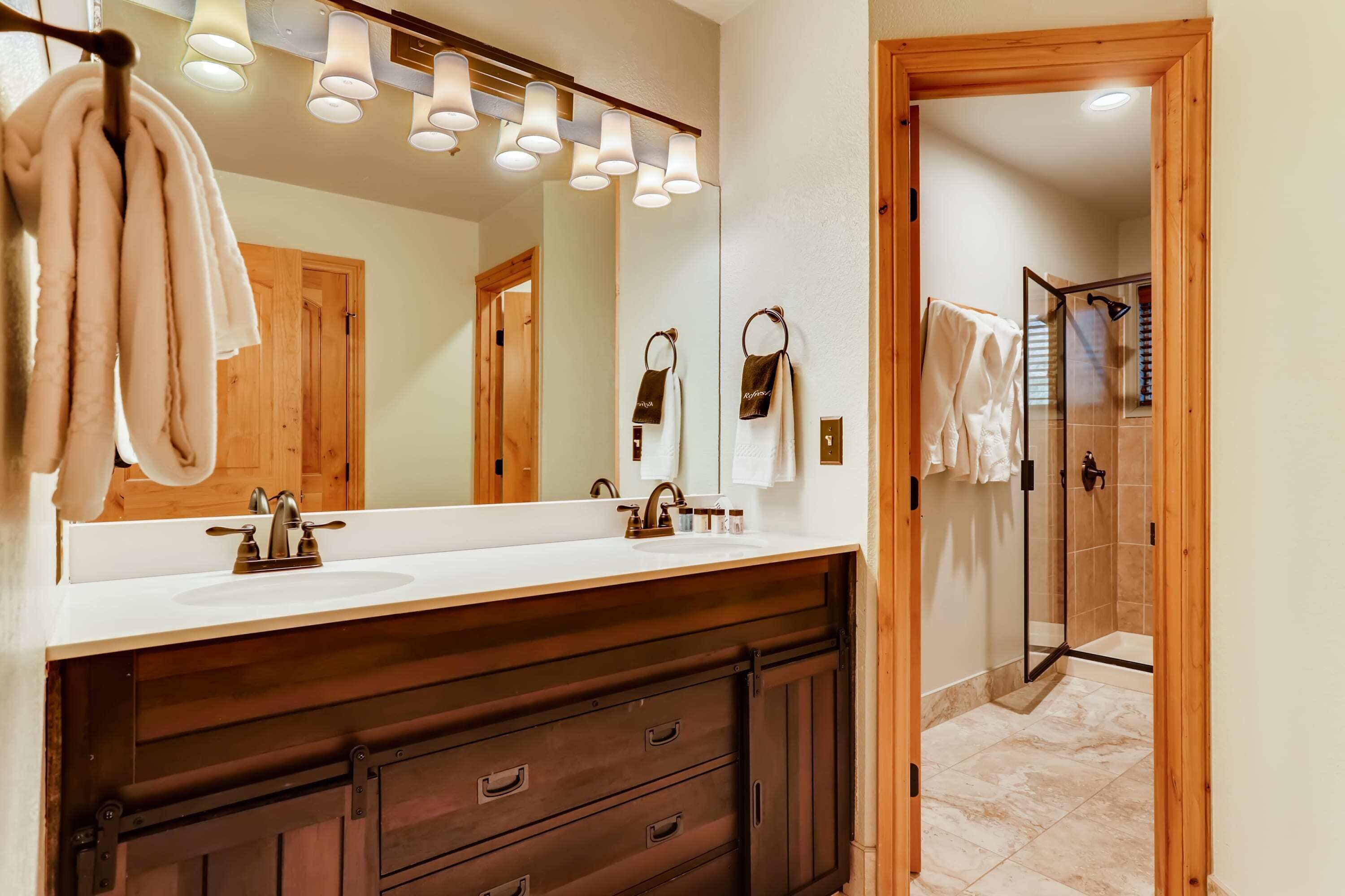A bathroom with a large mirror, two sinks, wooden cabinets, and a shower area.