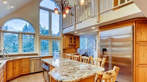 A spacious kitchen with a large island, wooden cabinets, and a stainless steel refrigerator. - Breck Town Lodge | In Town | Walkability (Breckenridge)