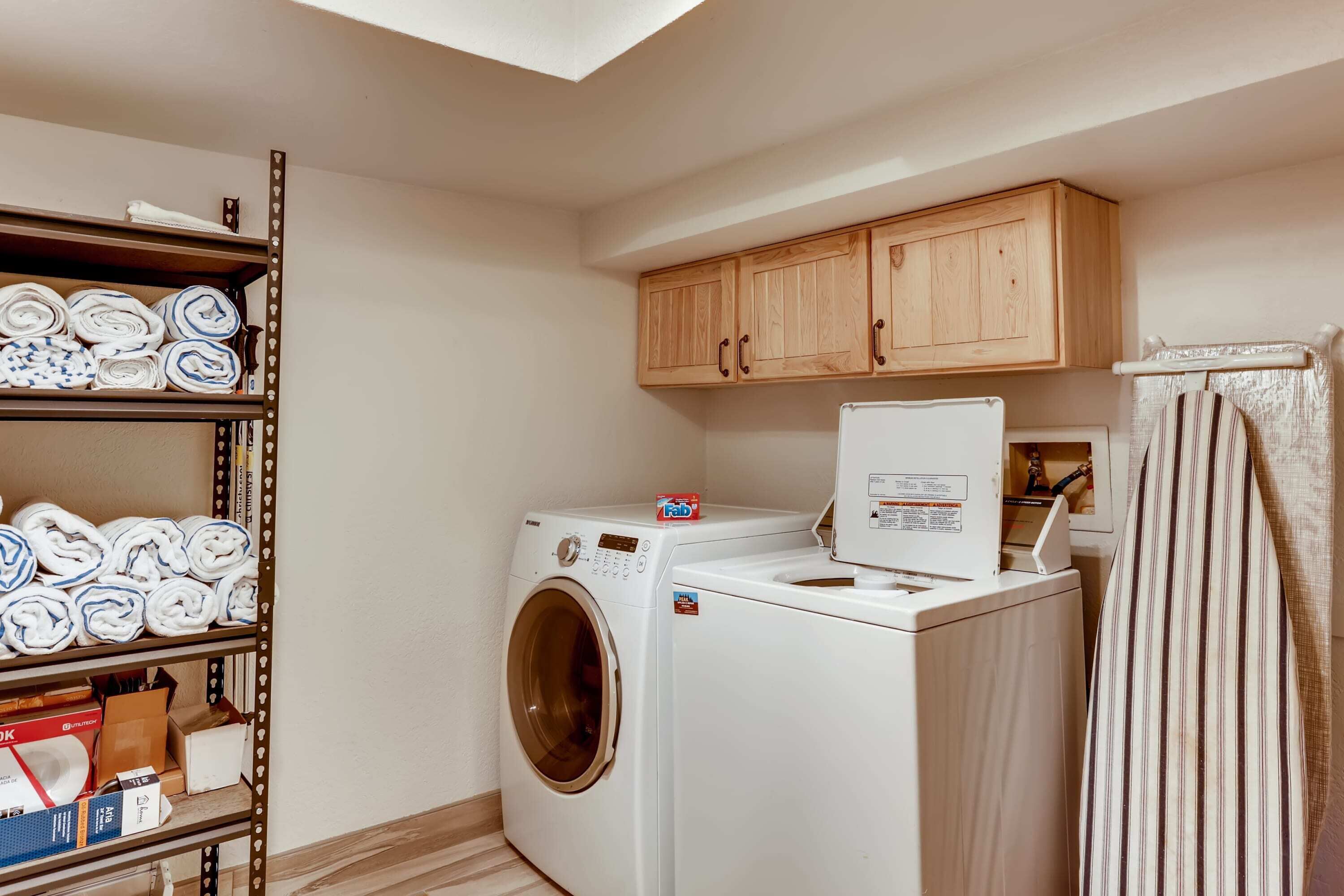 A laundry room with a washing machine, a dryer, wooden cabinets, and a shelf with folded towels.