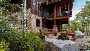 A two-story log cabin with a stone foundation, large windows, and a balcony with outdoor seating. - Castle Butenham by Cottonwood Lodging (Brighton)
