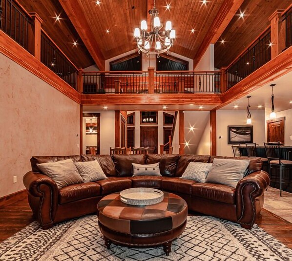 A spacious living room with a large L-shaped sectional sofa, a round ottoman, and a chandelier.