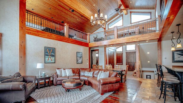 A spacious living room with a high ceiling, wooden beams, a fireplace, and a dining area with a bar. - Castle Butenham by Cottonwood Lodging (Brighton)