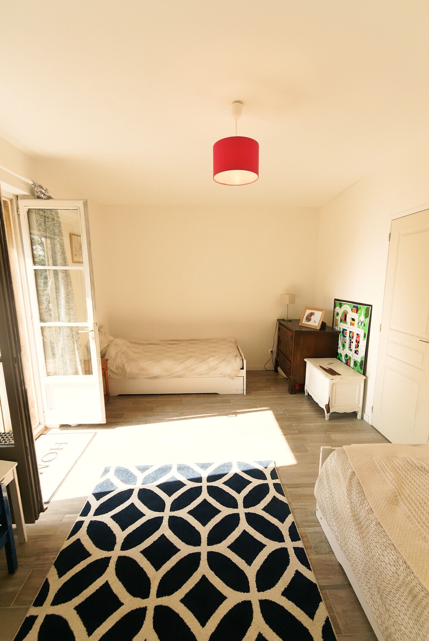 A bedroom with a bed, a dresser, a nightstand, a red hanging lamp, and a door leading to another room.
